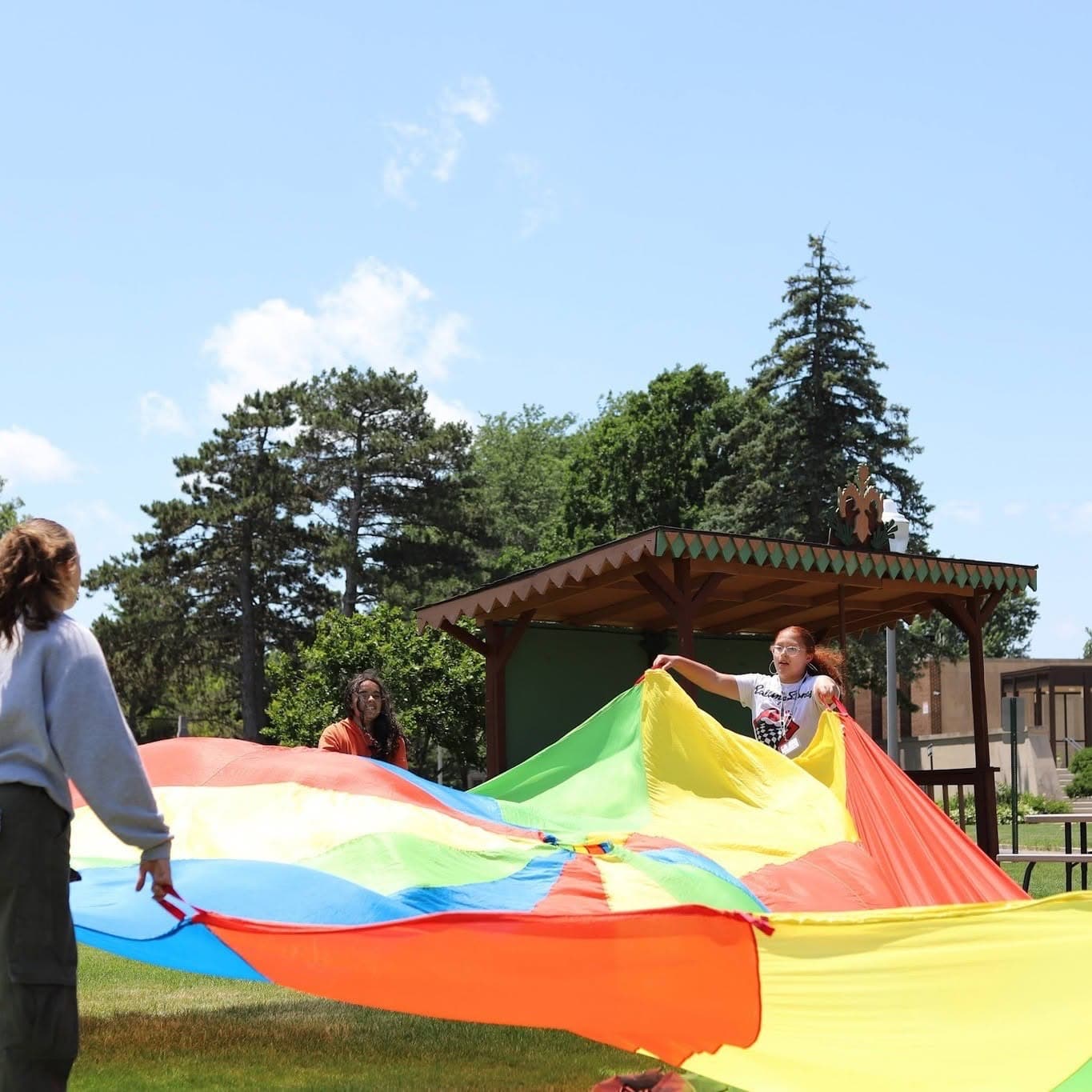 Children and leaders lift a rainbow parachute outdoors