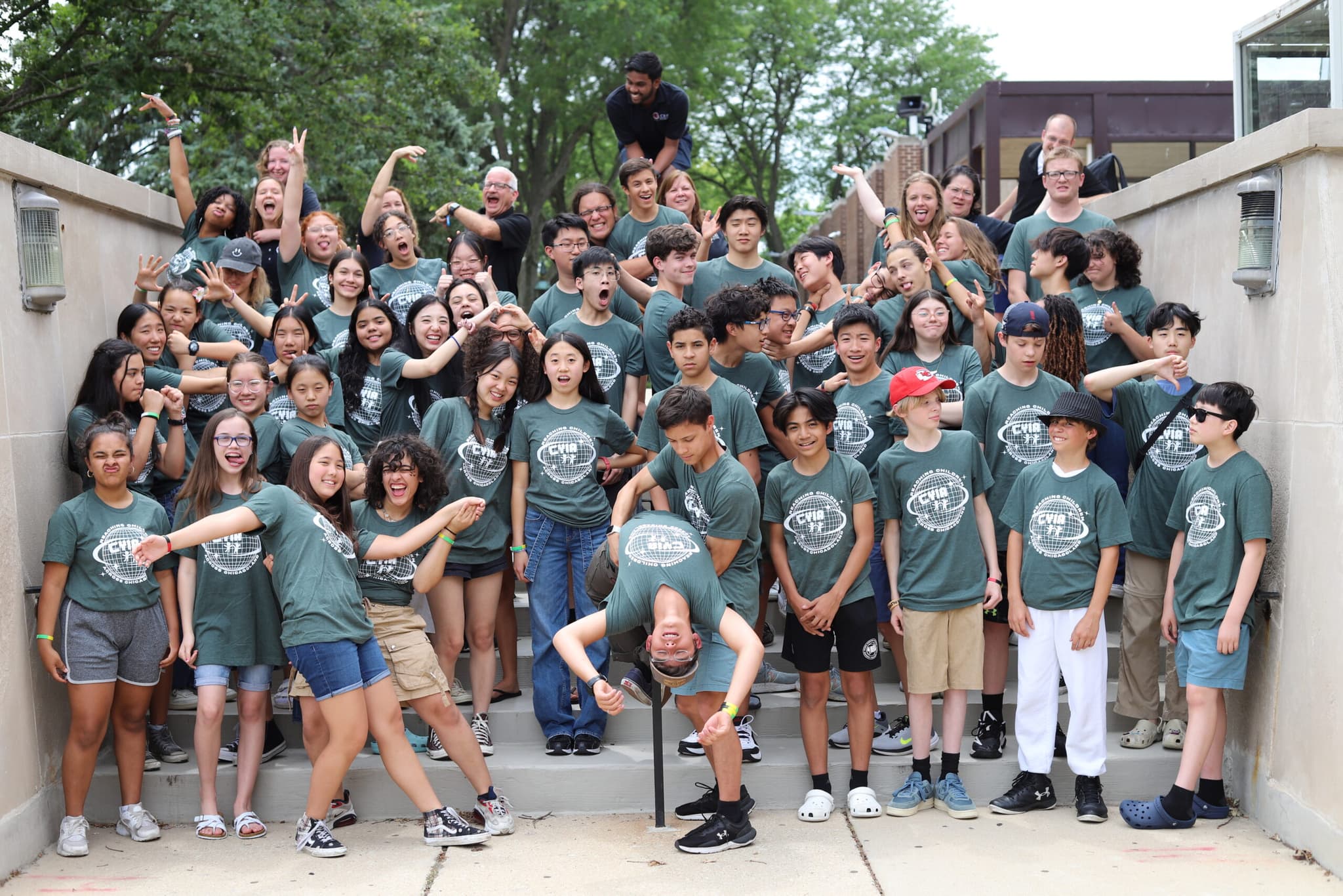 A large group of teenagers in matching green shirts cheer on a set of outdoor steps